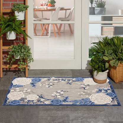 Rectangular outdoor entry rug with cream and blue floral pattern, blue border, on concrete by a glass door and potted plants.