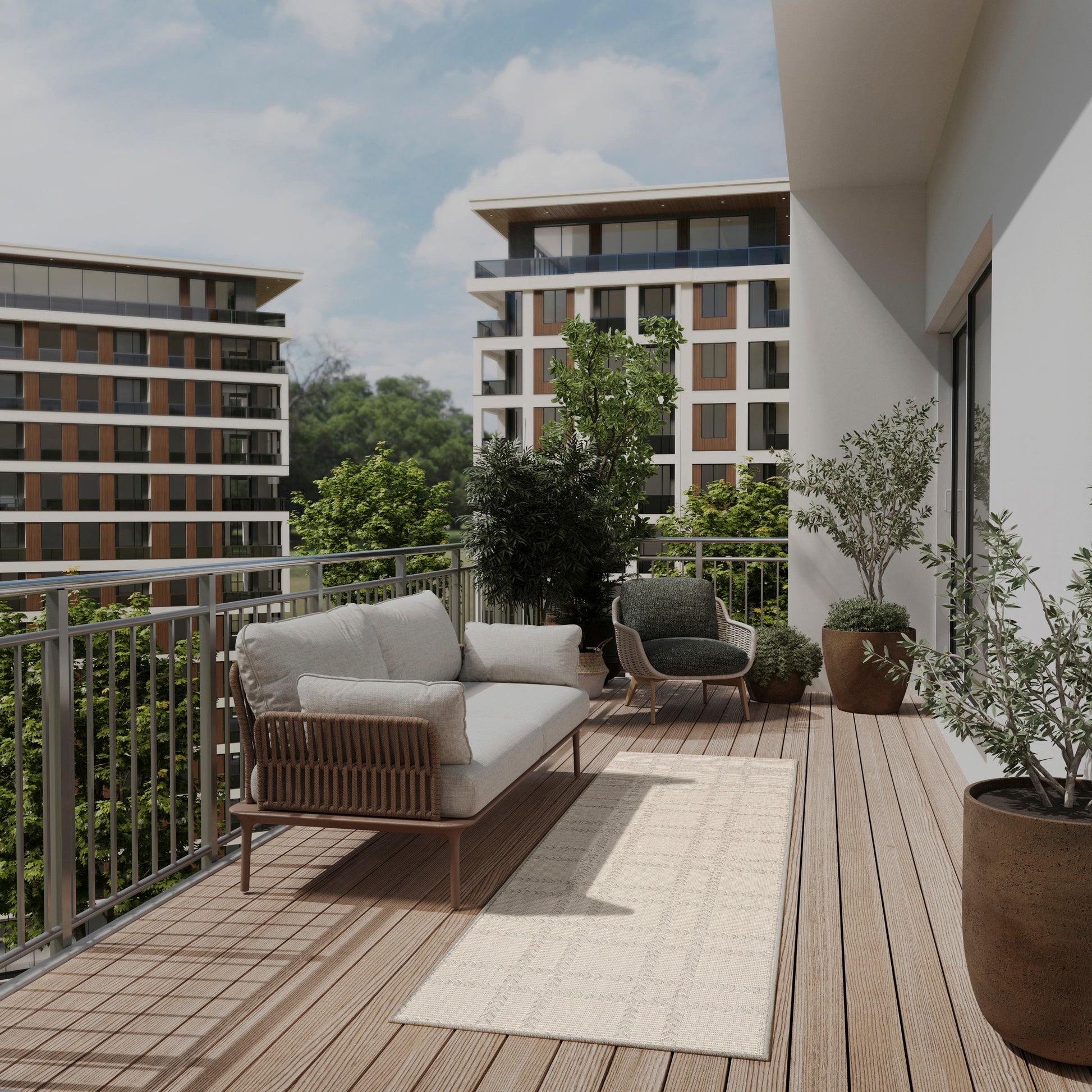 Sunlit balcony with cream-cushioned sofa, dark wicker chair, beige rug, potted plants, wooden deck, and buildings beyond.