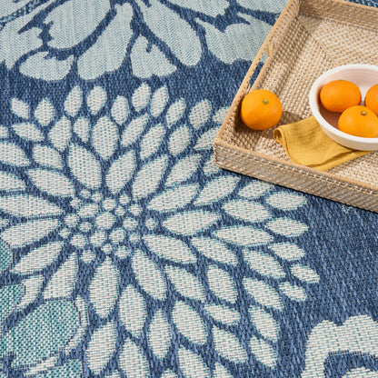 Blue & white woven rug with a large floral mandala pattern; wicker tray holding oranges & a yellow napkin.