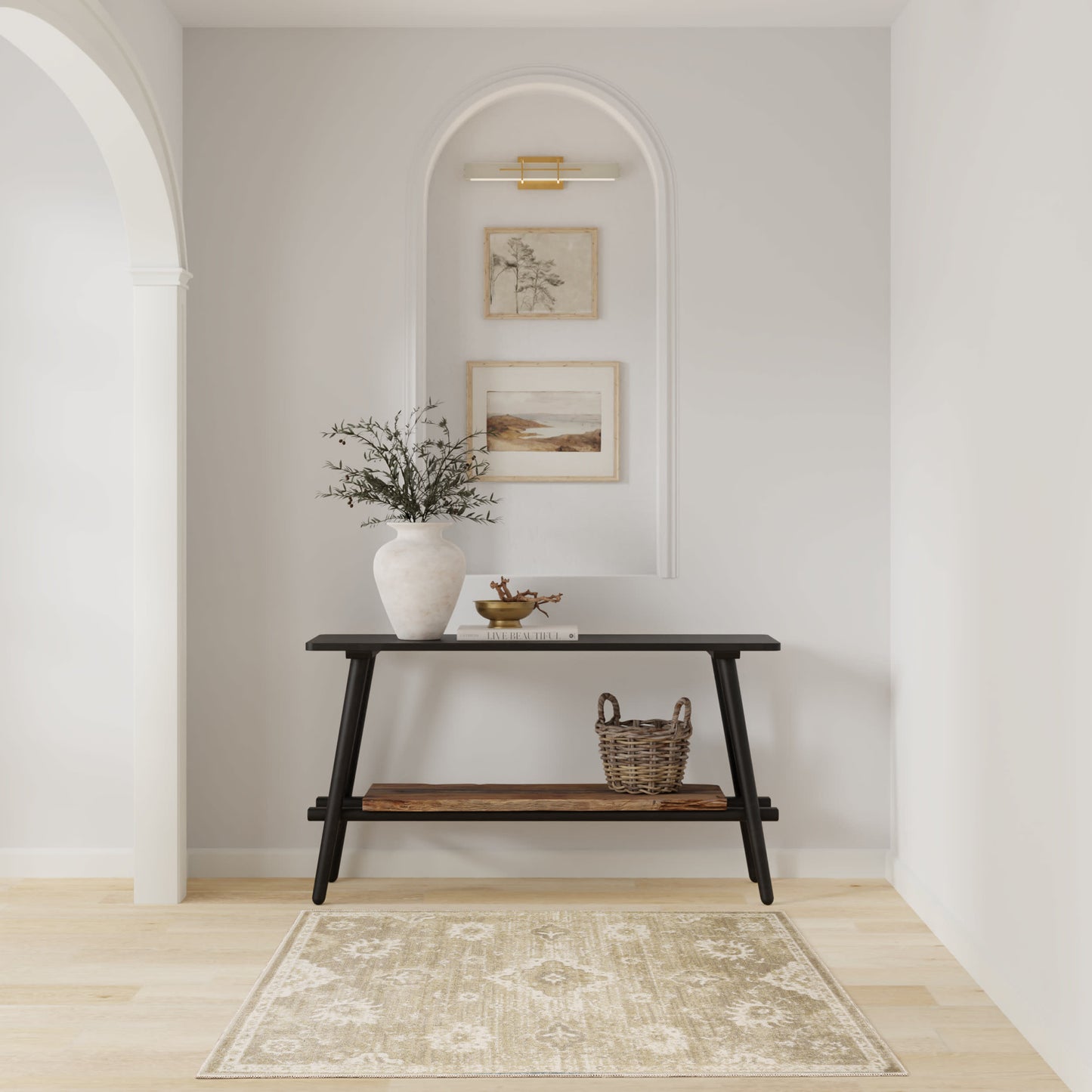 Dark wood console with angled legs in a light arched alcove; vase with branches, framed art, sconce lighting, beige rug.