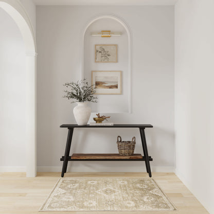 Dark wood console with angled legs in a light arched alcove; vase with branches, framed art, sconce lighting, beige rug.