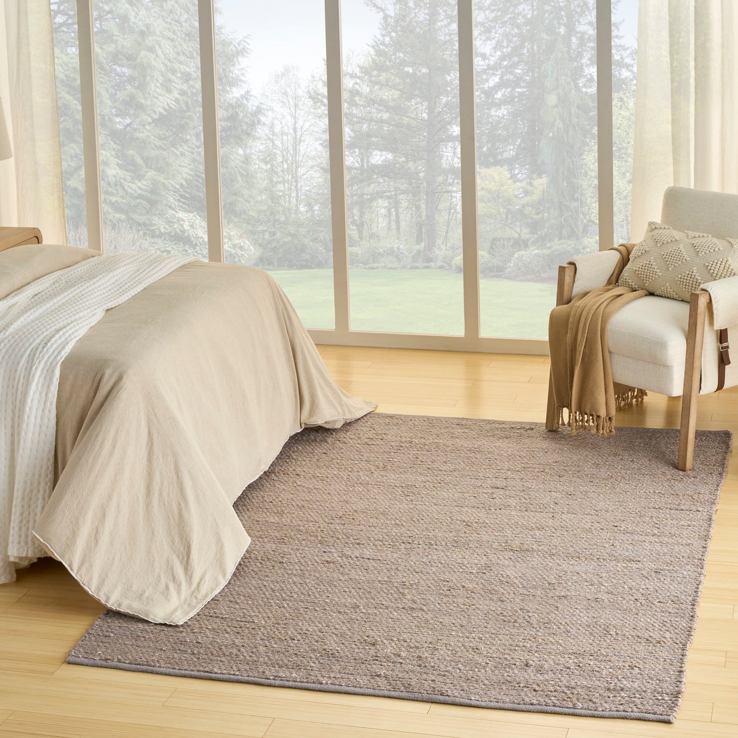 Beige rug with a textured gray pattern on light wood floors beside a cushioned chair by floor-to-ceiling windows.