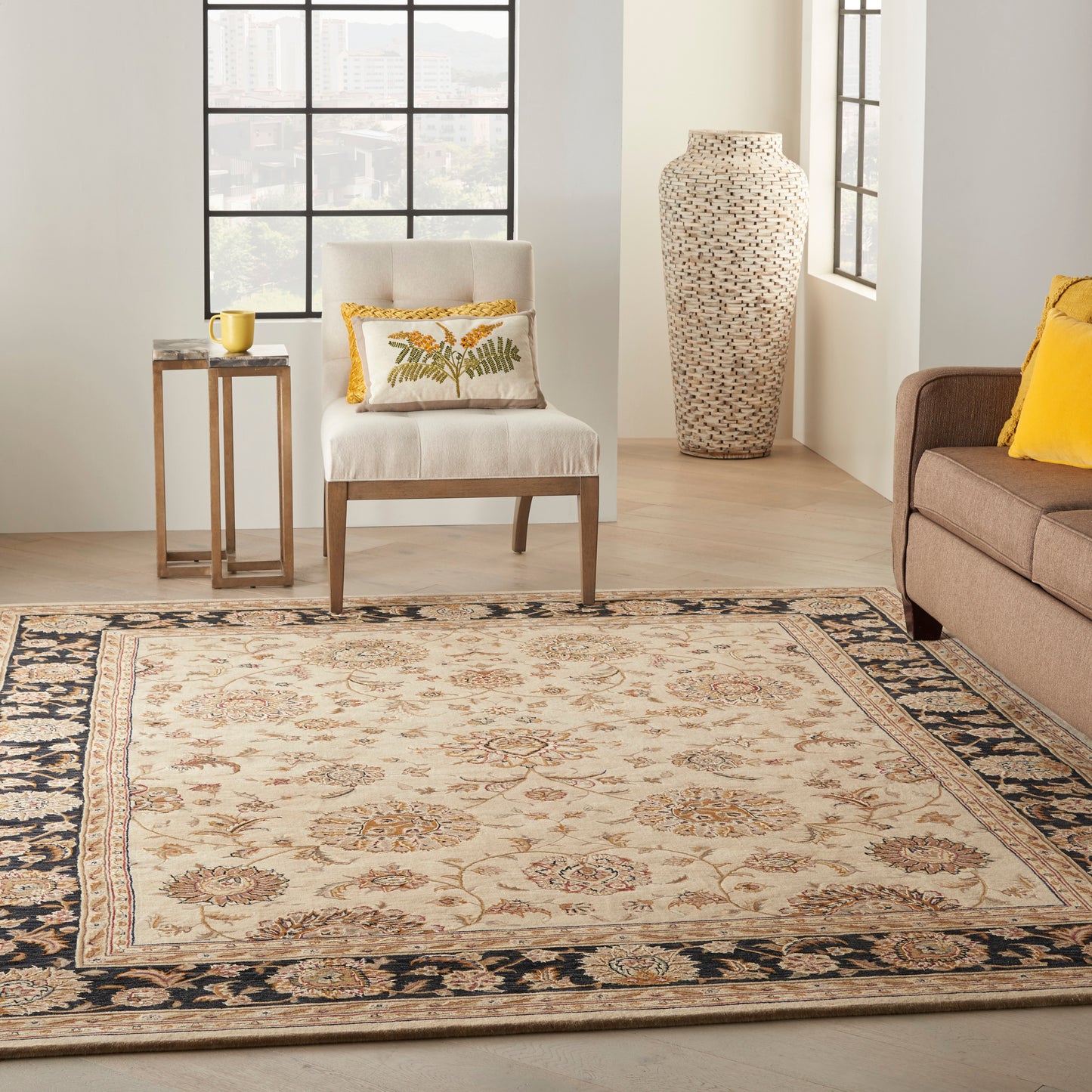 Oriental-style beige area rug with gold florals and navy border in a bright living room; beige chair, yellow cushions, vase.
