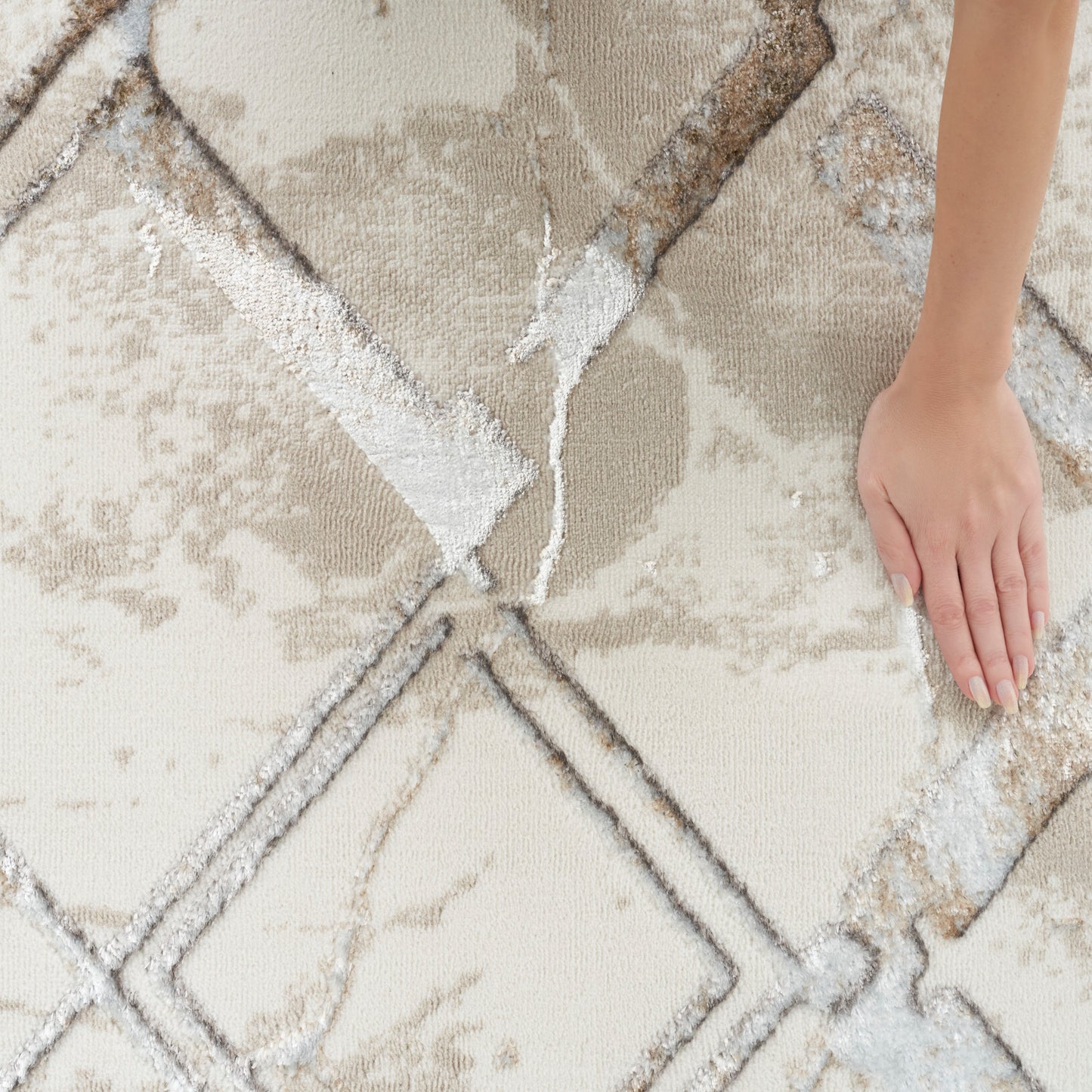 Hand resting on a beige and gray geometric rug with diamond shapes and plush, textured pile.
