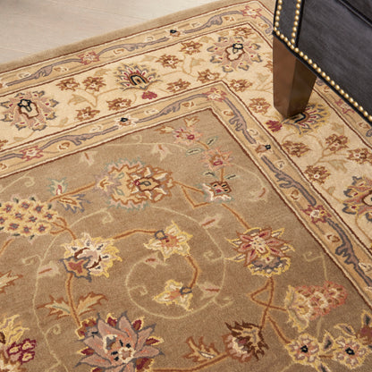 Beige oriental area rug with pastel floral motifs and blue-bordered edges on a wood floor beside a nailhead-studded chair leg.