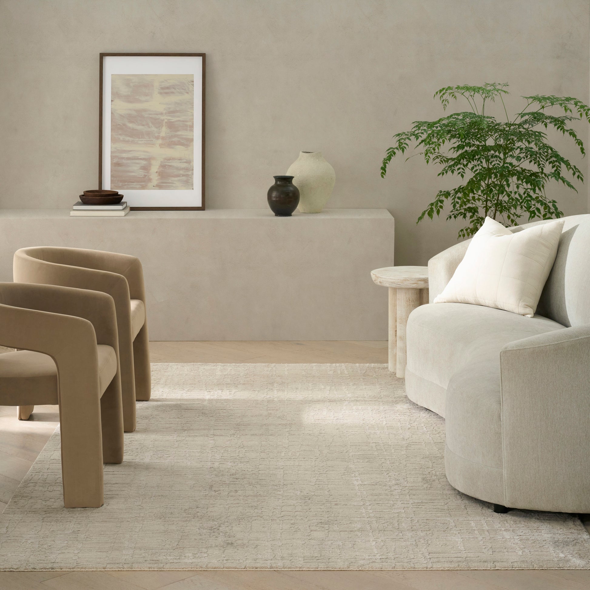 Neutral living room featuring a modern 5' x 8' rug on the floor, with taupe armless chairs, a rounded beige sofa, a light wood side table, art, ceramic vases, and a plant.