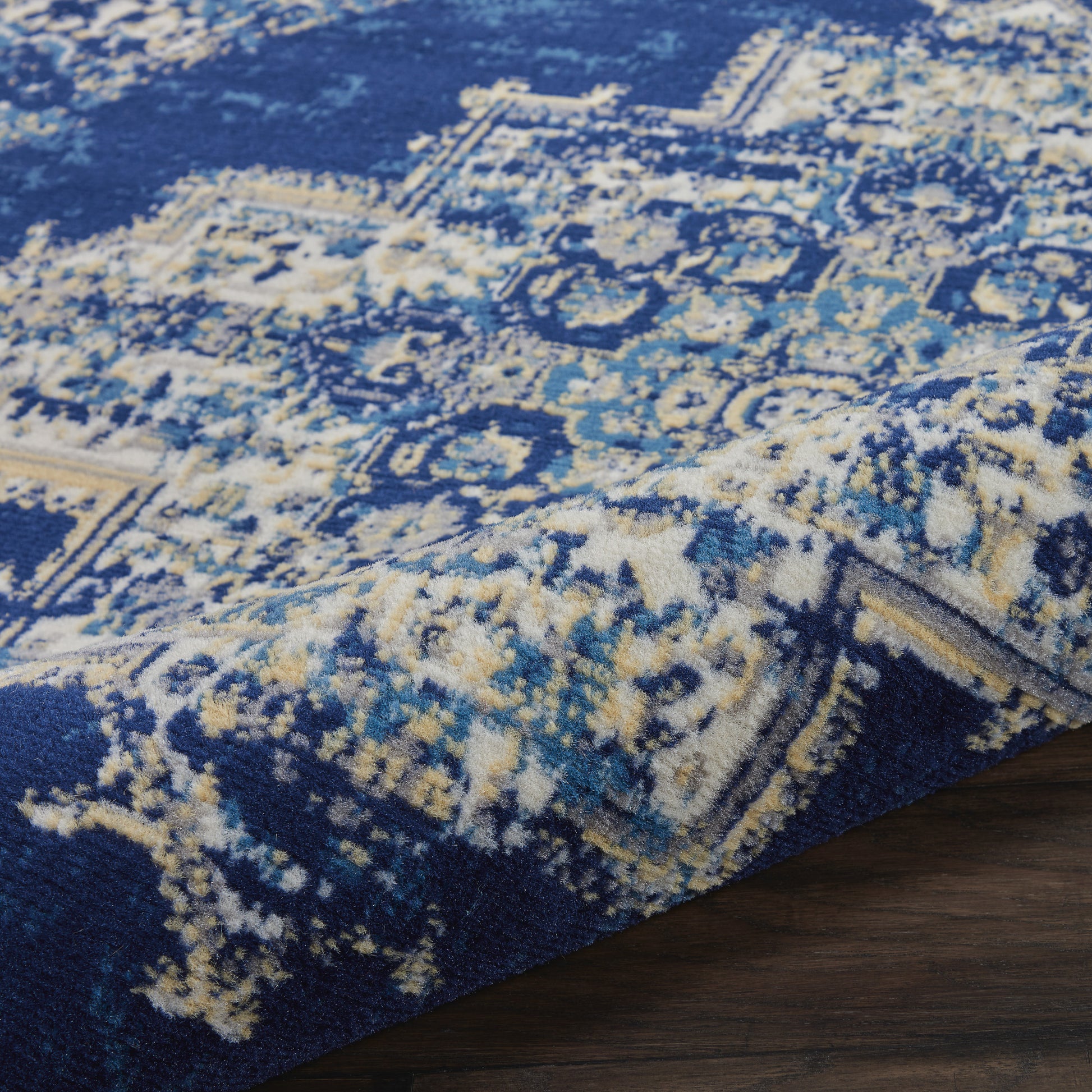 Blue oriental round rug, 5 ft diameter, with cream and pale yellow motifs on a plush pile, shown on a dark wood floor.