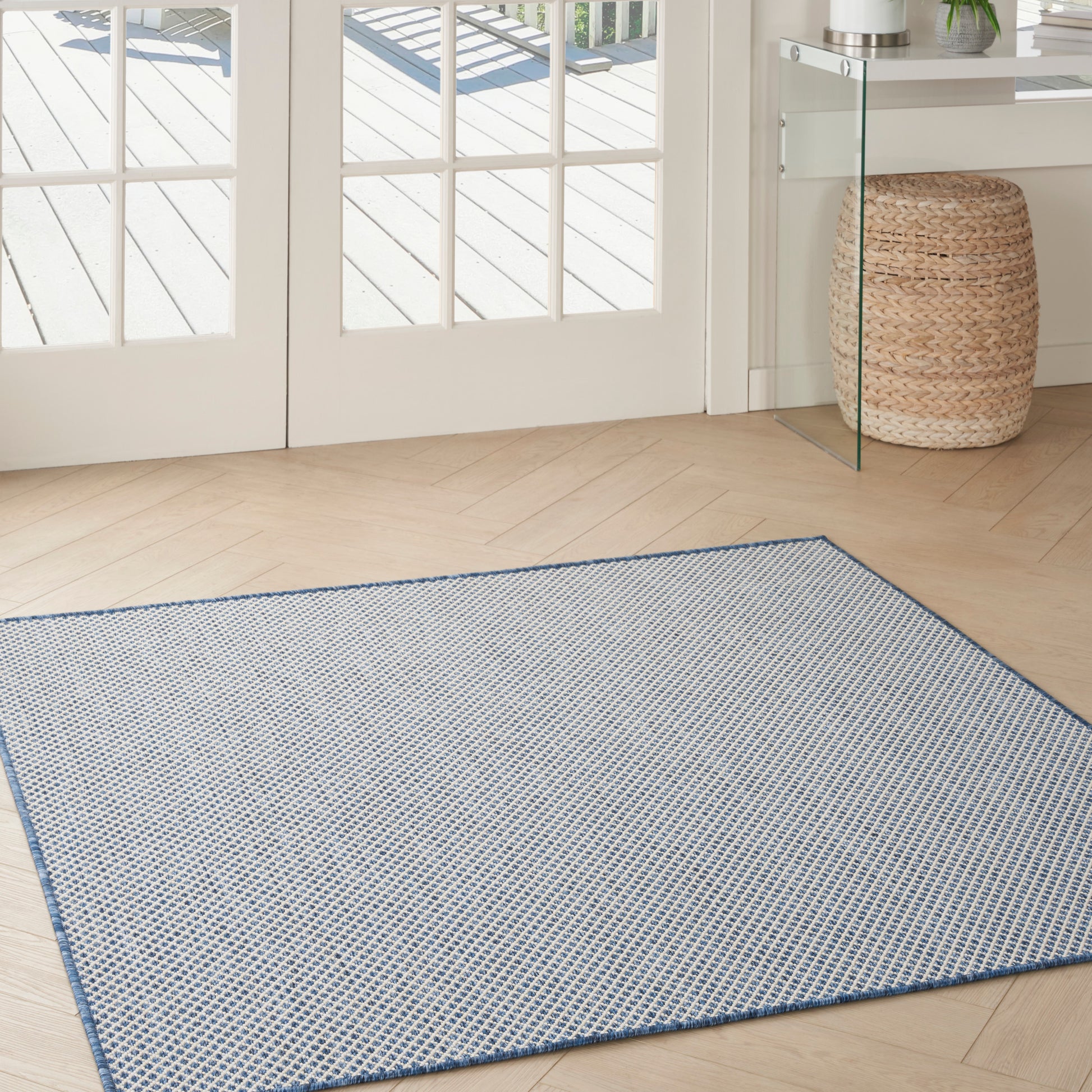 Blue and white woven area rug with a blue border on light wood floor near glass doors.