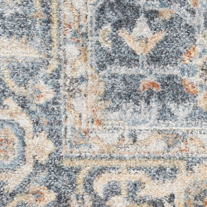 Close-up of a blue-gray and beige patterned rug with ivory scrolls and floral motifs, plush pile.