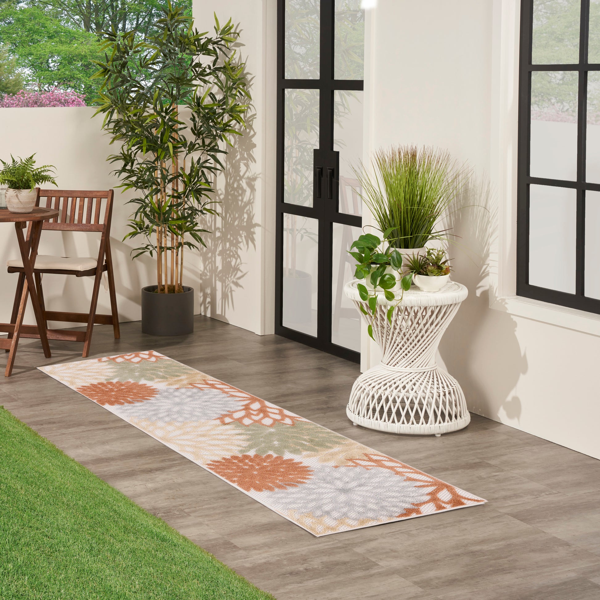 Long runner rug with orange and gray floral motifs on beige, beside wicker table and potted plants on wood floor.