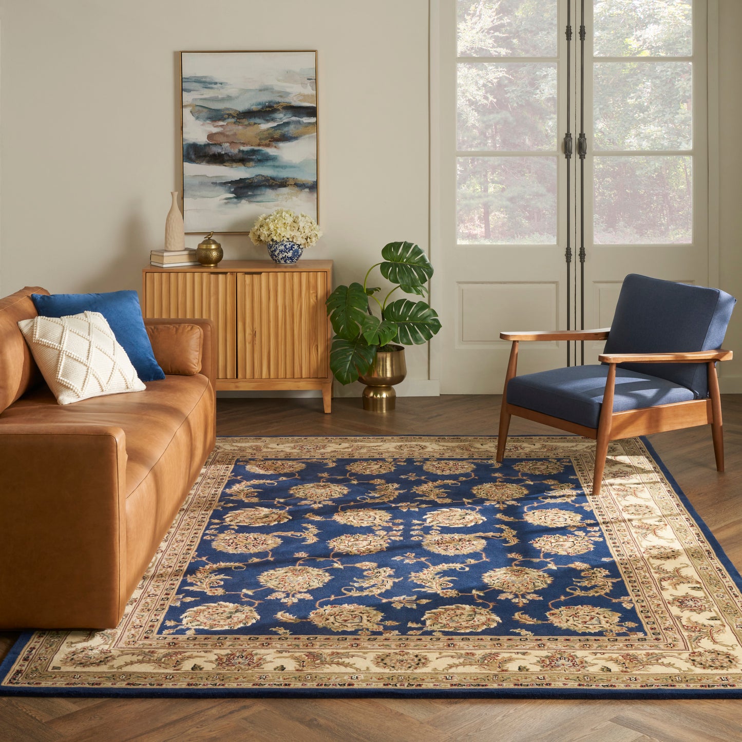 Blue ornate oriental rug anchors a living room with a brown leather sofa, mid-century wooden chair, and a wooden sideboard.