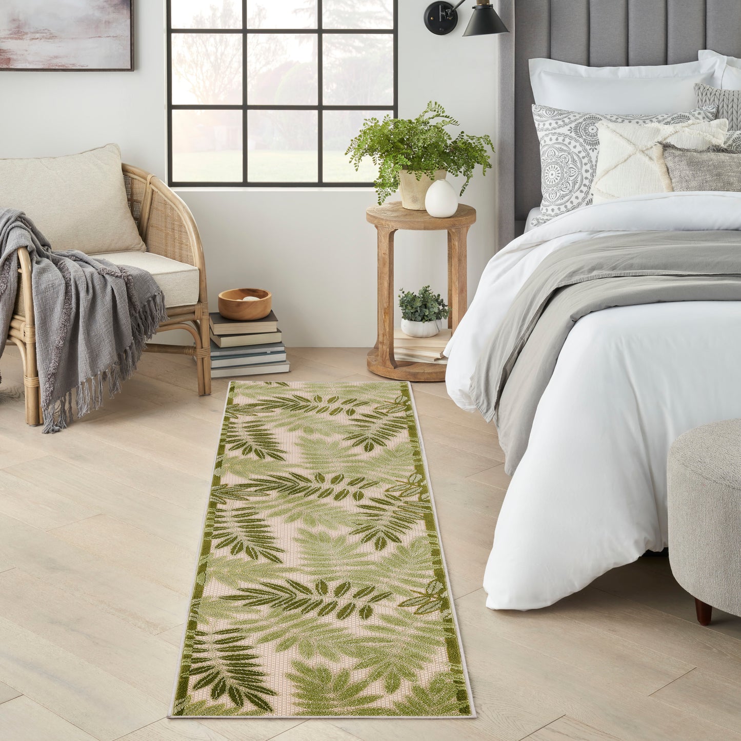 Rectangular fern-patterned runner rug in green tones with a dark green border on pale wood floor in a bright bedroom.
