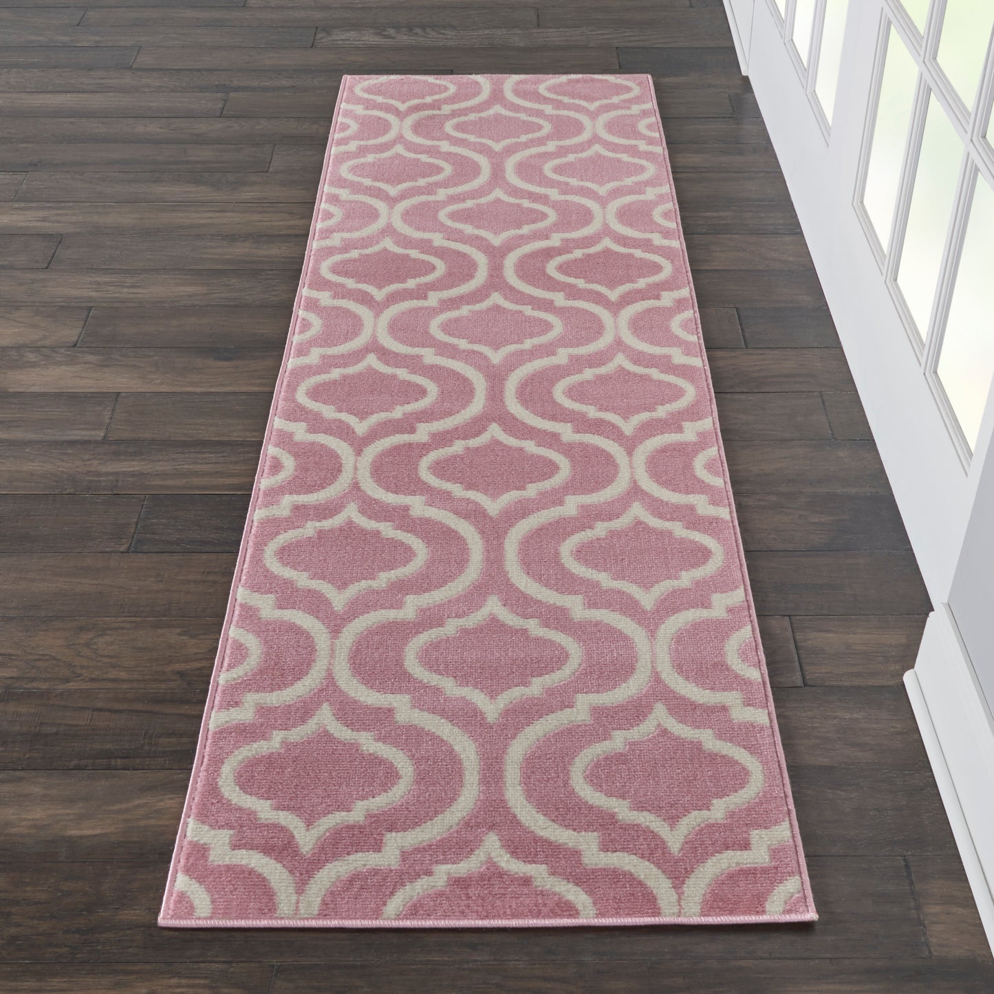 Pink runner rug with cream trellis pattern on dark wood floor; soft, decorative hallway accent.