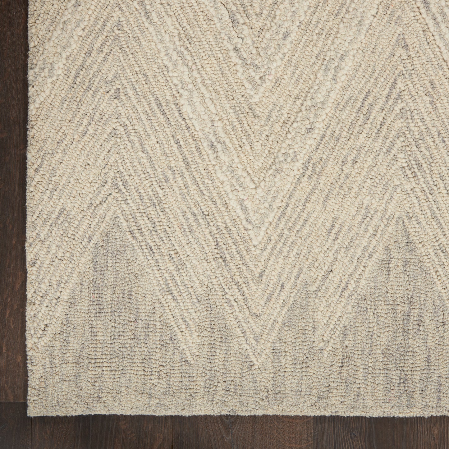 Beige chevron-patterned textured rug on dark wood floor; low-pile tufted loops with subtle shading.