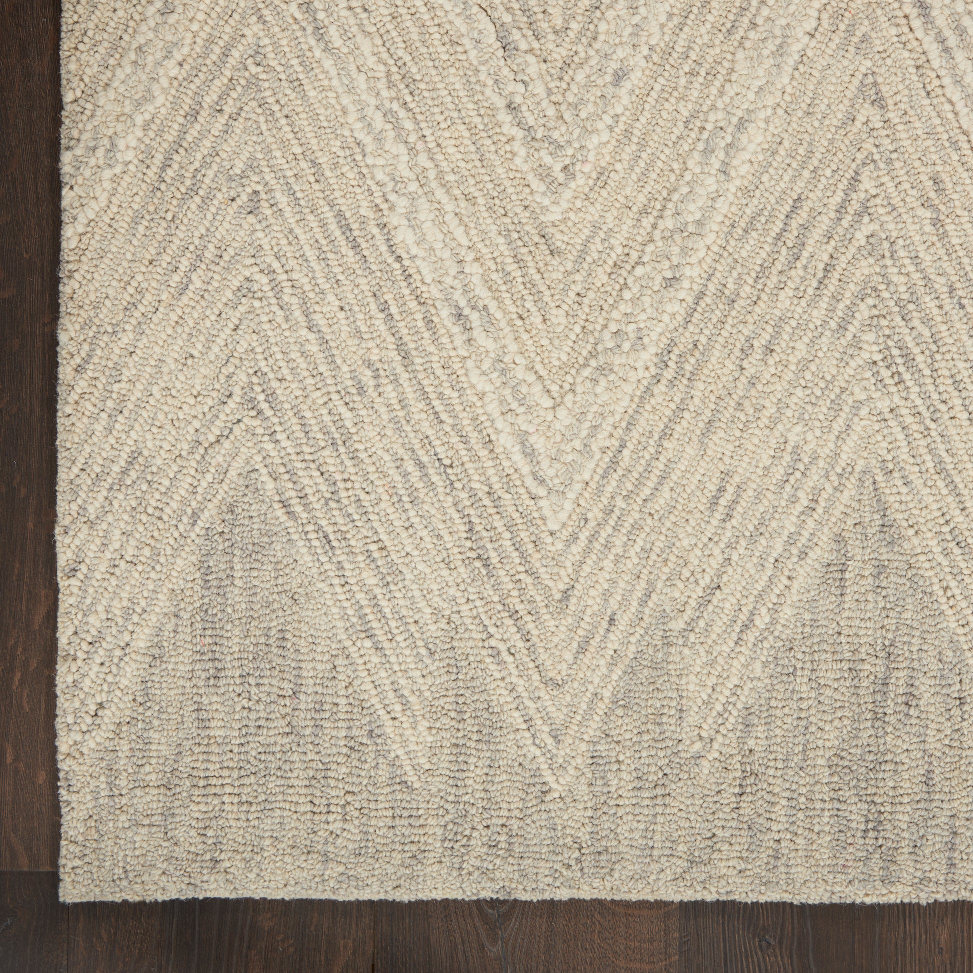 Beige chevron-patterned textured rug on dark wood floor; low-pile tufted loops with subtle shading.