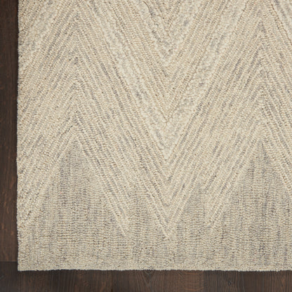 Beige chevron-patterned textured rug on dark wood floor; low-pile tufted loops with subtle shading.