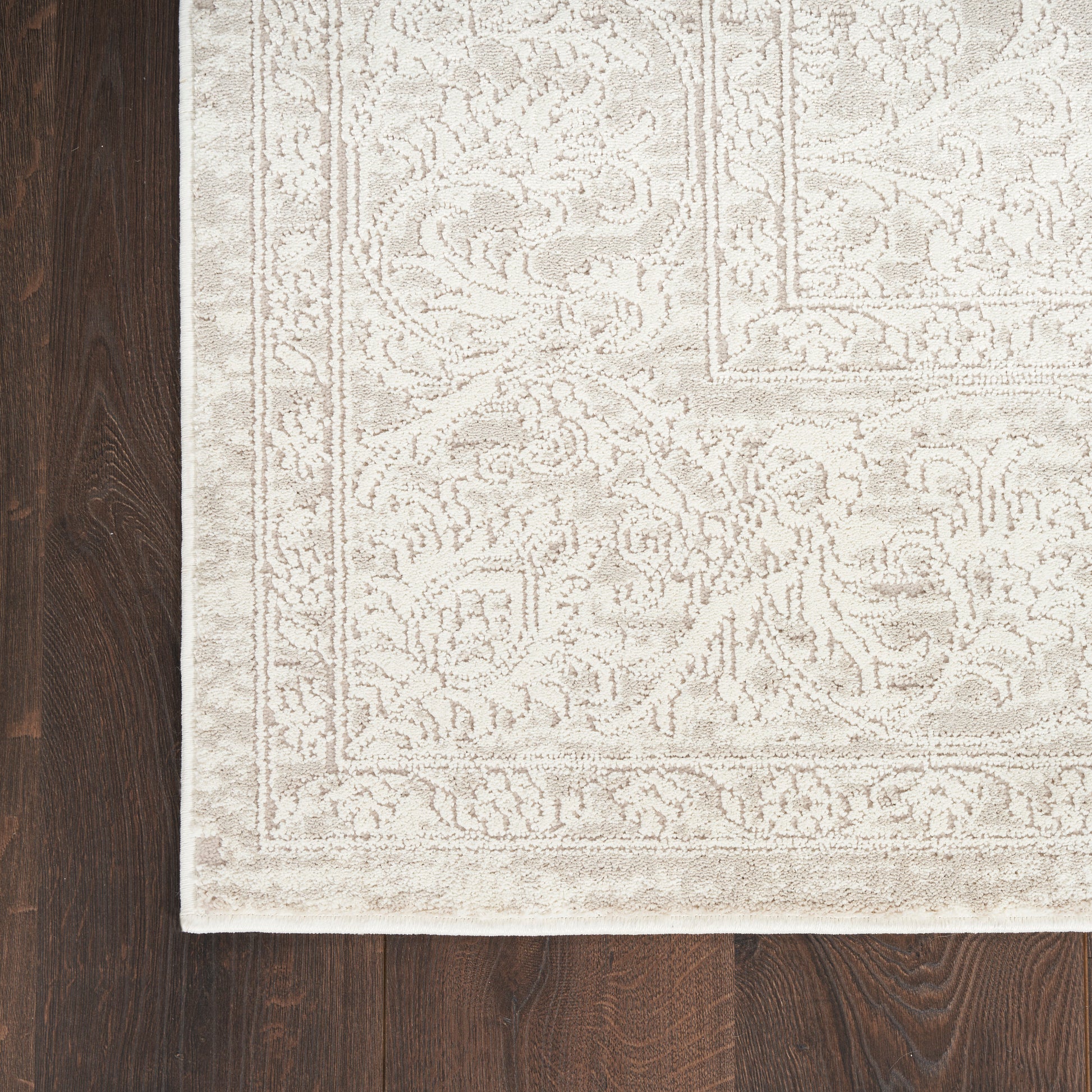 Cream oriental rug with an intricate ivory floral border, laid on a dark wooden floor.