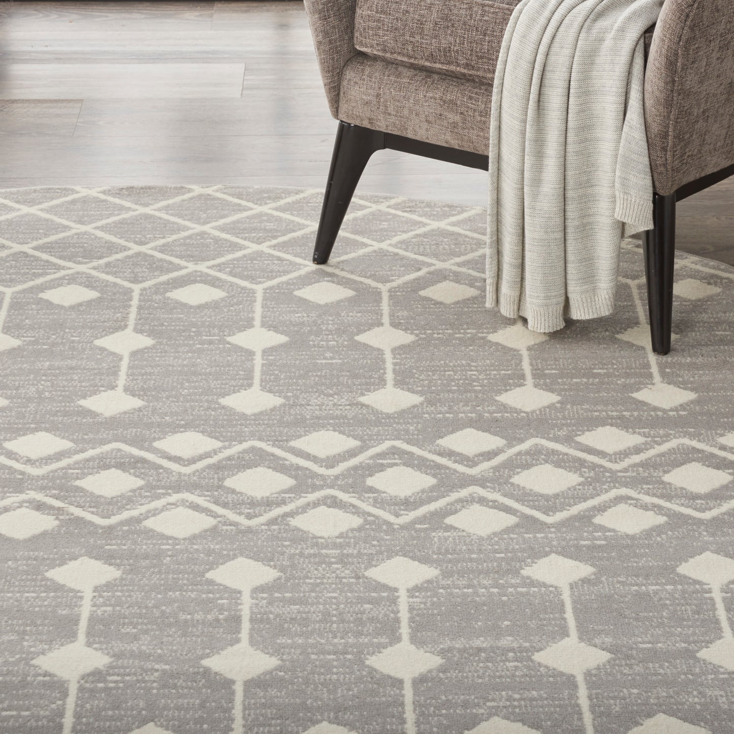 Neutral gray woven area rug with cream diamond trellis pattern under a brown armchair and a cream throw blanket.