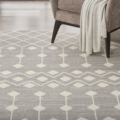 Neutral gray woven area rug with cream diamond trellis pattern under a brown armchair and a cream throw blanket.