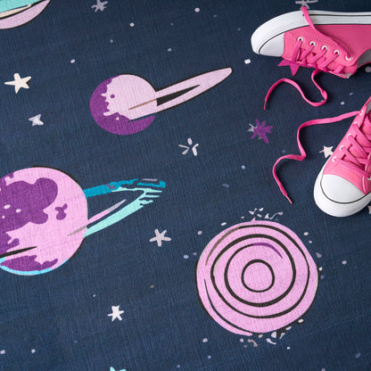 Space-themed blue rug featuring pink and purple planets, rings and stars; pink sneakers with white toe caps sit at the edge.