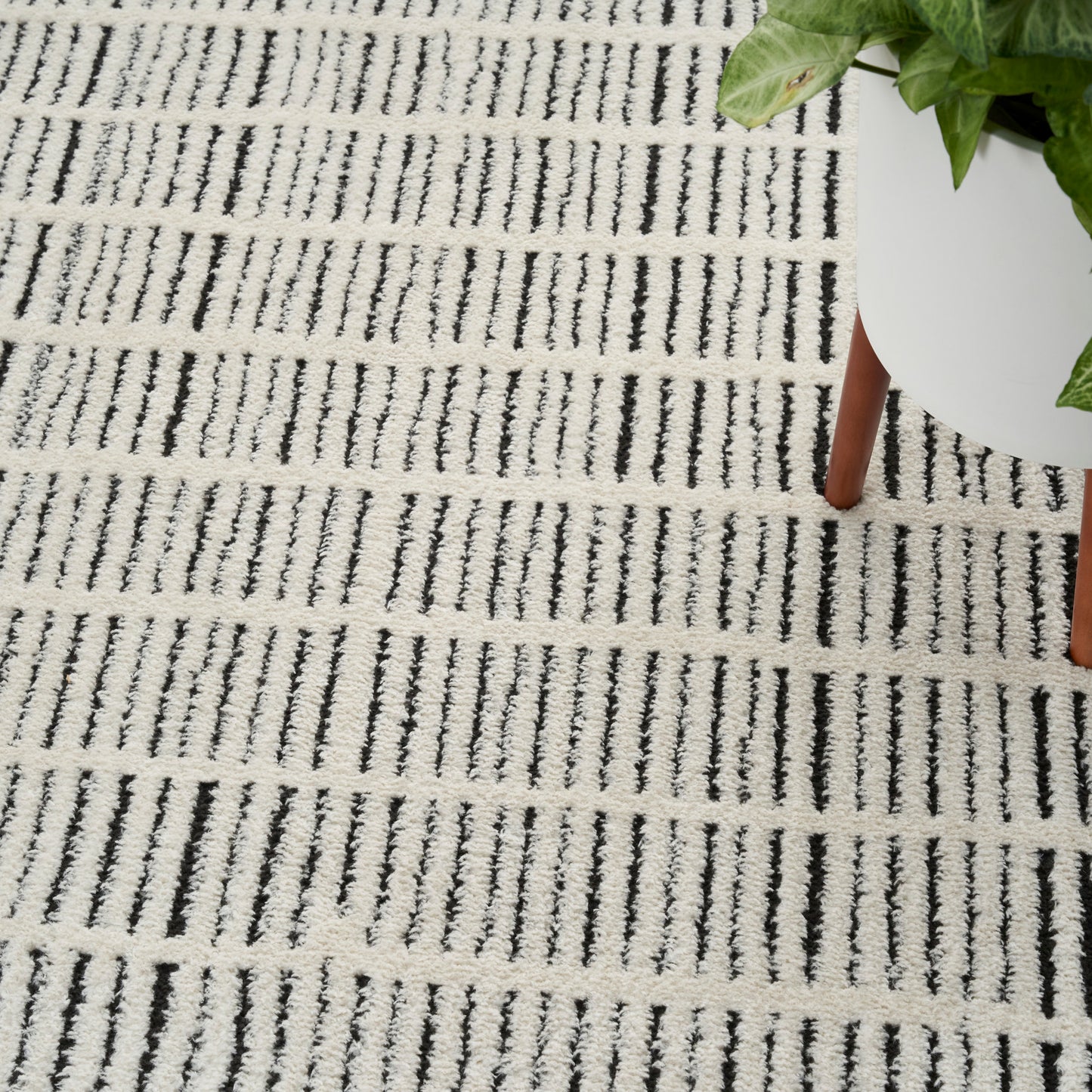 White textured rug with black vertical brush-stroke stripes; partial view of a white round table with wooden legs.