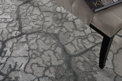 Gray textured area rug with an abstract pattern; beige tufted stool with studded trim and black tapered leg, with a book on top.