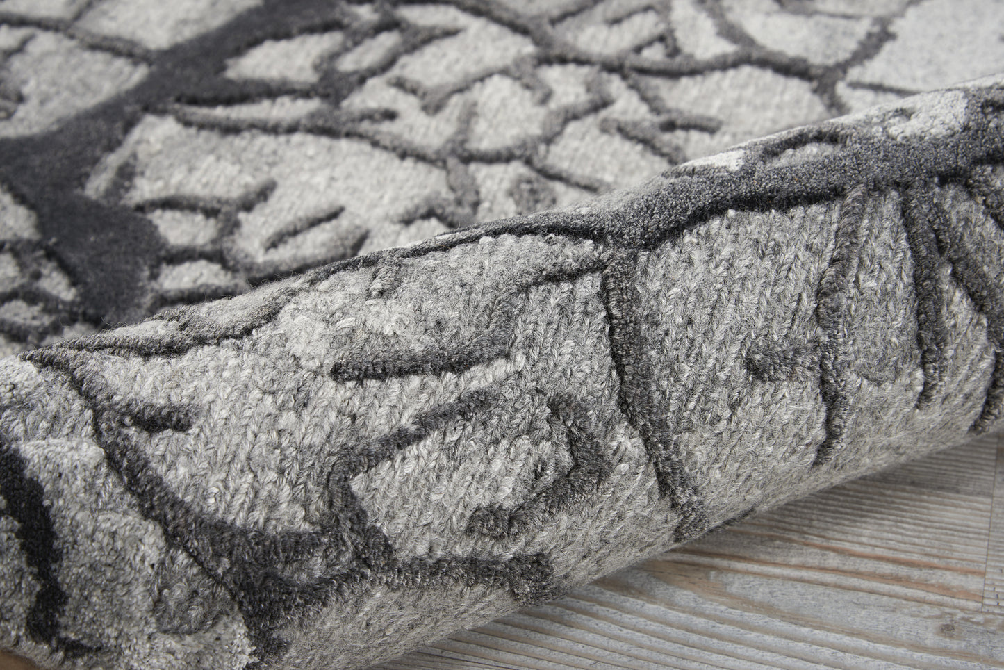Gray abstract patterned rug with charcoal lines, plush pile, rolled edge on light wood floor.