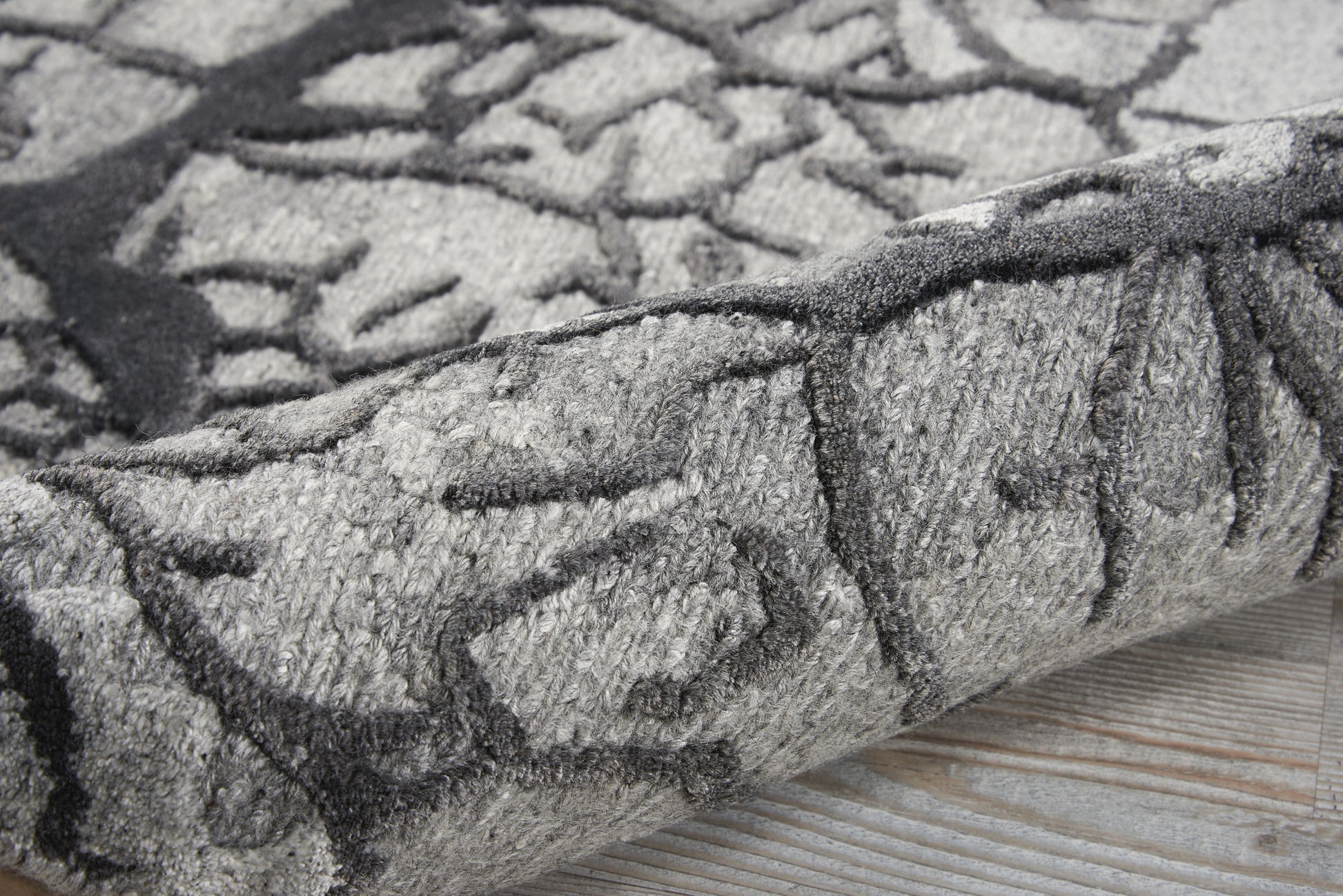 Gray abstract patterned rug with charcoal lines, plush pile, rolled edge on light wood floor.