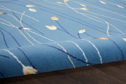 Blue rug with abstract white lines and yellow leaf-like accents, wool-like pile, folded edge on dark wood floor.