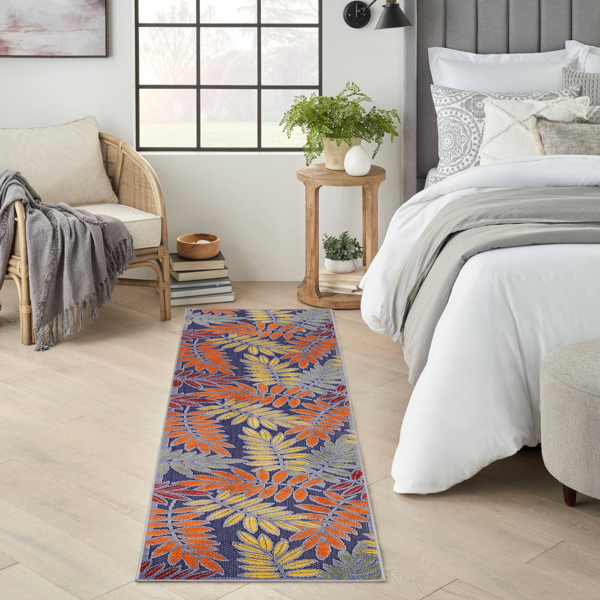 Narrow woven outdoor runner rug with blue background and orange-yellow botanical leaves.