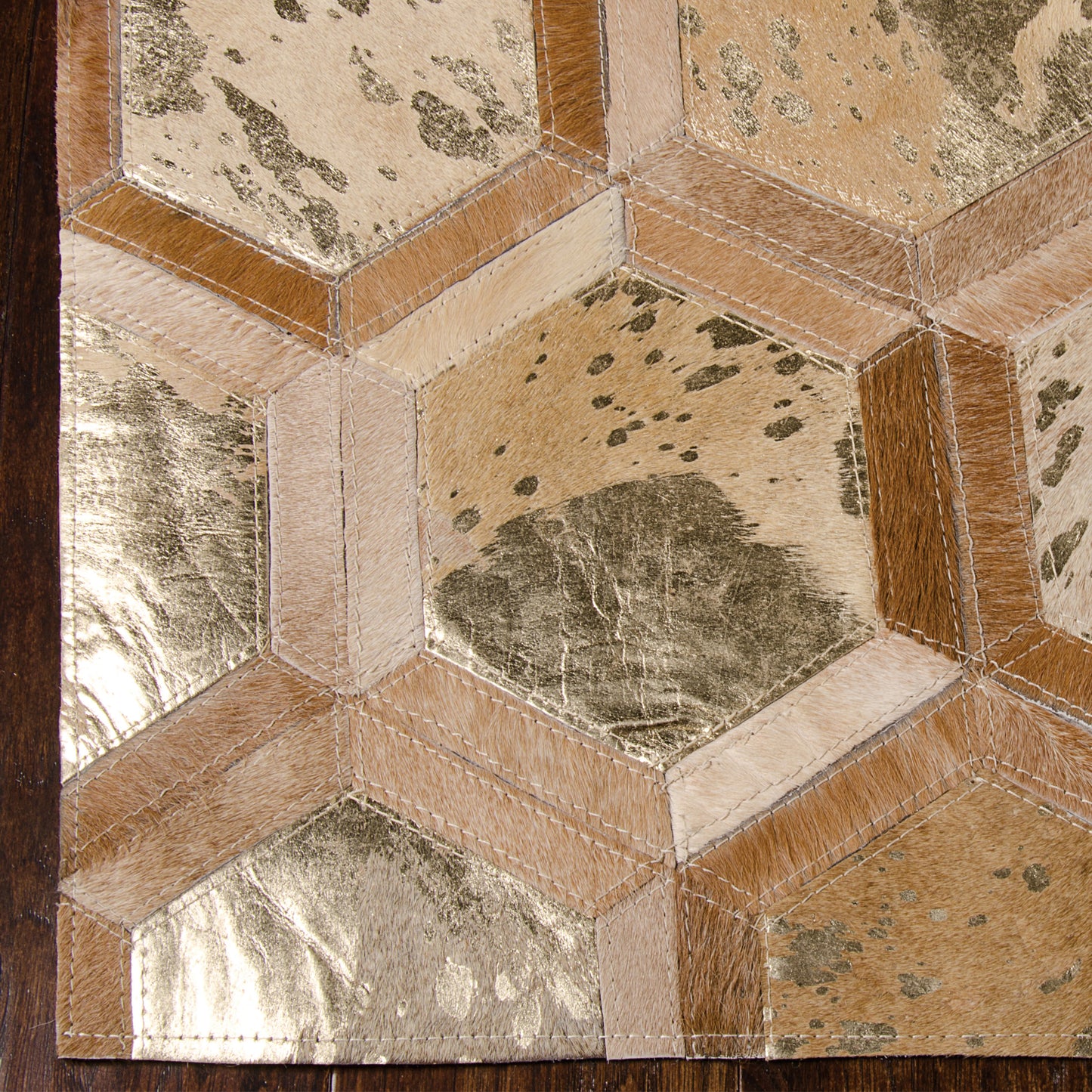 Close-up of metallic gold hexagonal motifs forming a geometric honeycomb on a rug, with tan borders and pink-beige stitching.