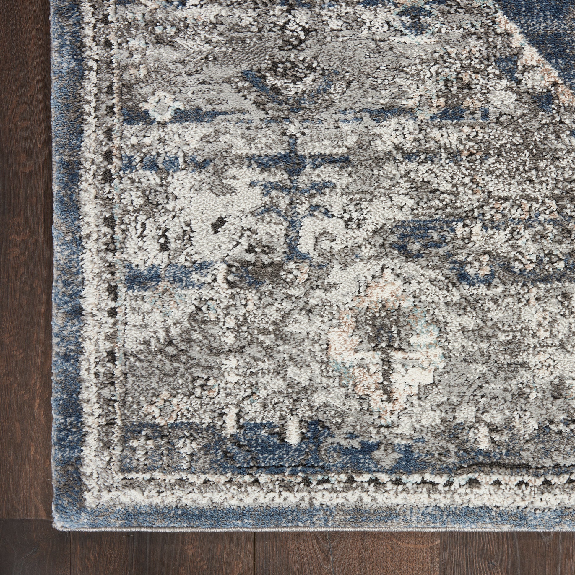 Distressed blue-gray oriental area rug with cream accents on dark wood floor; decorative border.