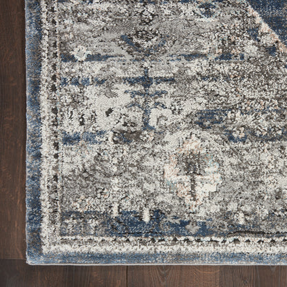 Distressed blue-gray oriental area rug with cream accents on dark wood floor; decorative border.
