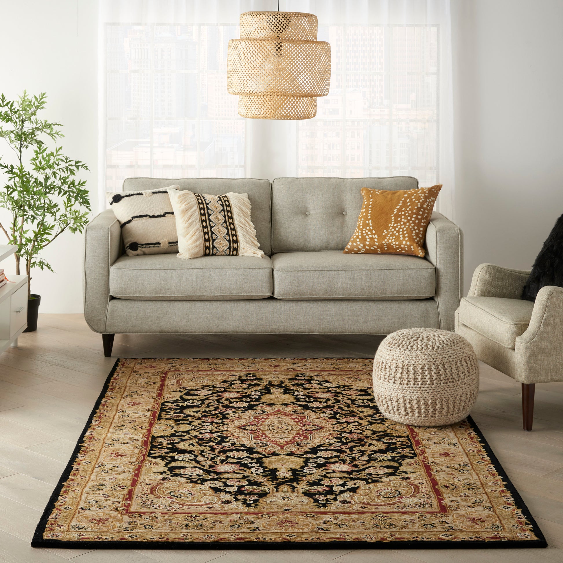 Boho living room with a gray tufted sofa, patterned cushions, woven pendant light, beige pouf, and an ornate oriental rug.