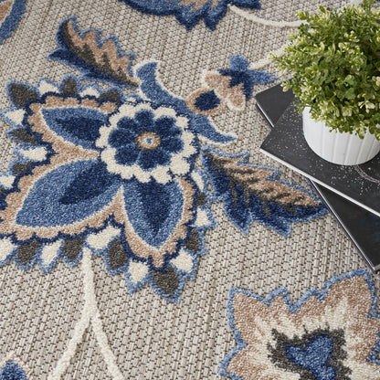 Blue, beige, and cream floral area rug with woven texture; large blue flower motif and potted plant on dark notebook.