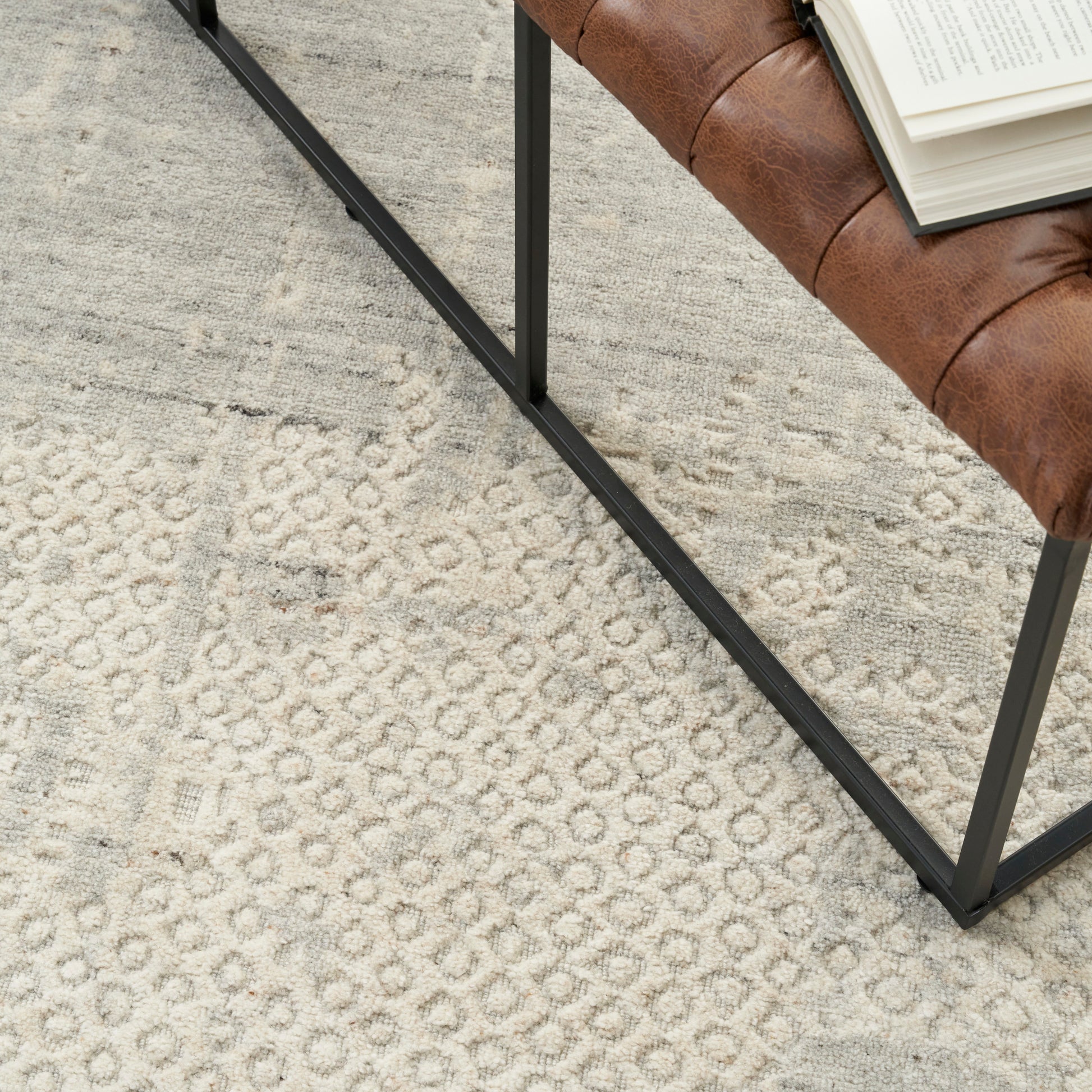 Brown leather upholstered chair with black metal frame on a beige patterned rug; open book resting on seat.