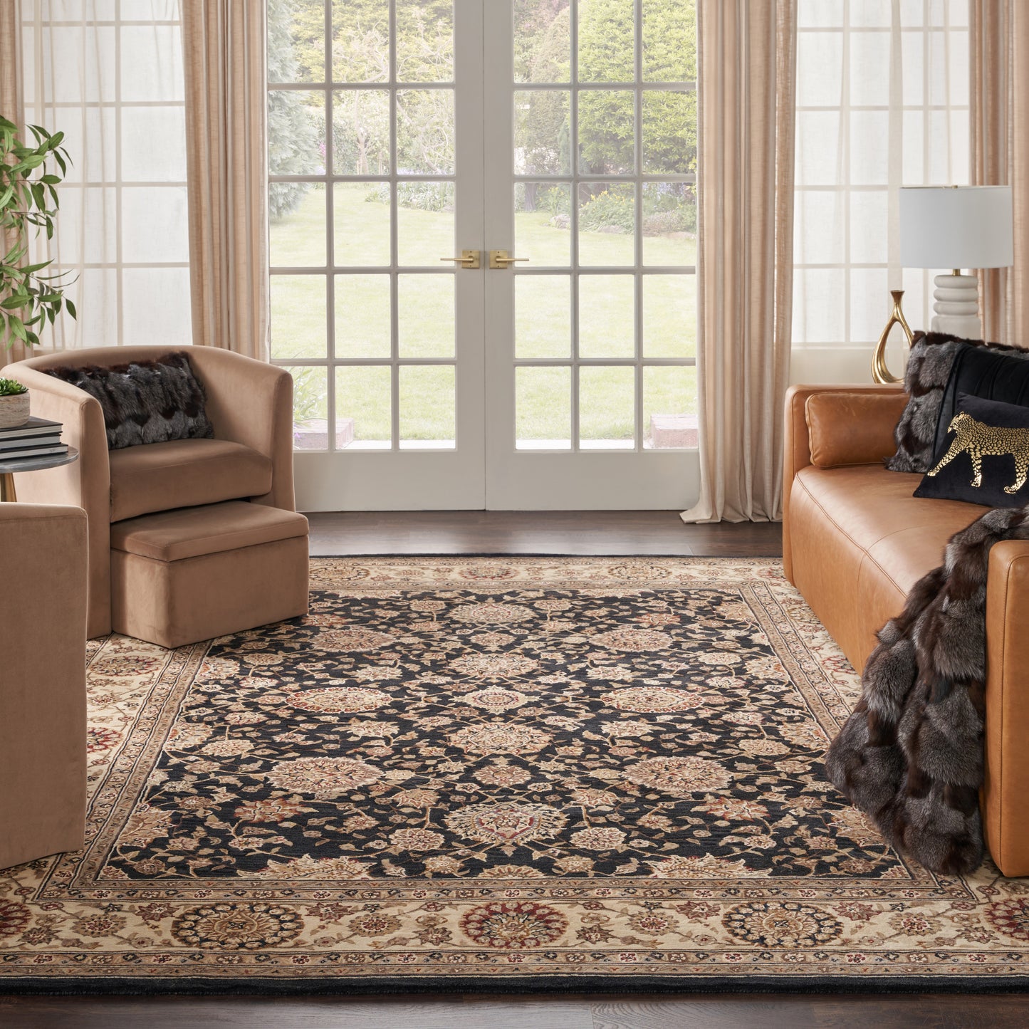 Cozy living room with tan leather sofa & chair, ornate navy & beige Persian rug, cream curtains & French doors.