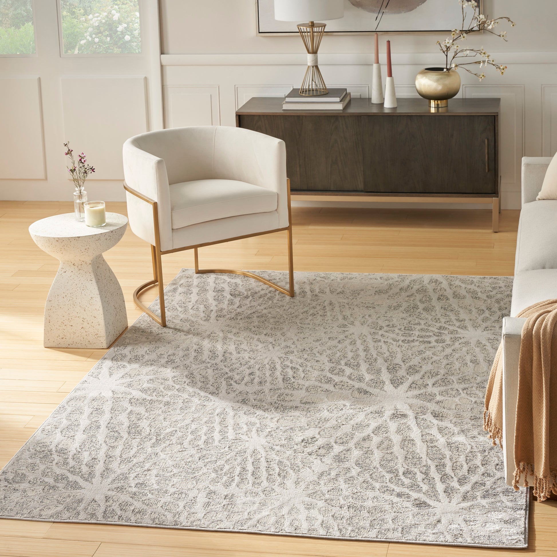 Neutral-toned modern rug 4' x 6' with a light gray pattern, placed in a living room alongside a cream upholstered armchair on a brass frame and a dark wood sideboard.