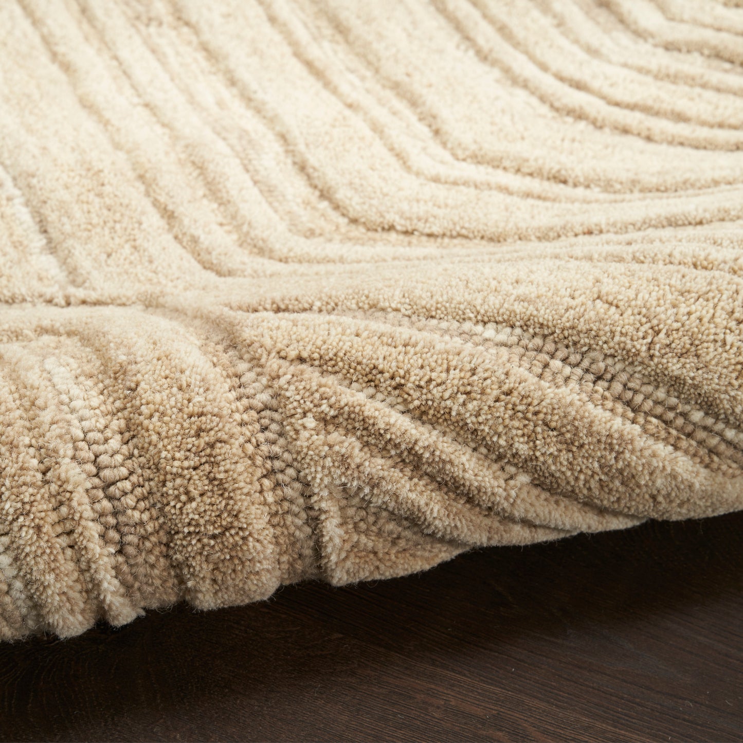 Beige plush rug with ribbed, looped texture on dark wood floor.