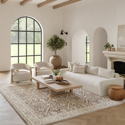 Bright neutral living room with cream sofa, white armchairs, arched window, wood beams, patterned rug, and coffee table.