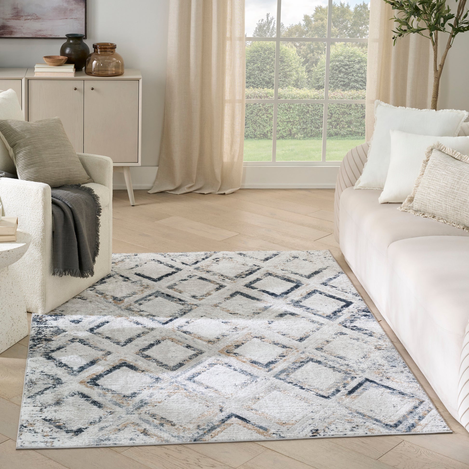 Neutral living room with a blue-grey geometric diamond-pattern area rug, cream sofa, light wood floor and beige curtains.