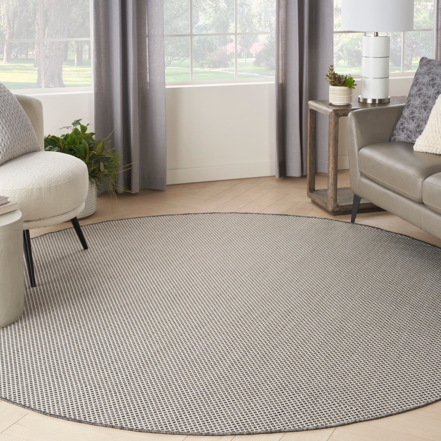 Round gray woven area rug in a modern living room with sofa, chair, and plants.