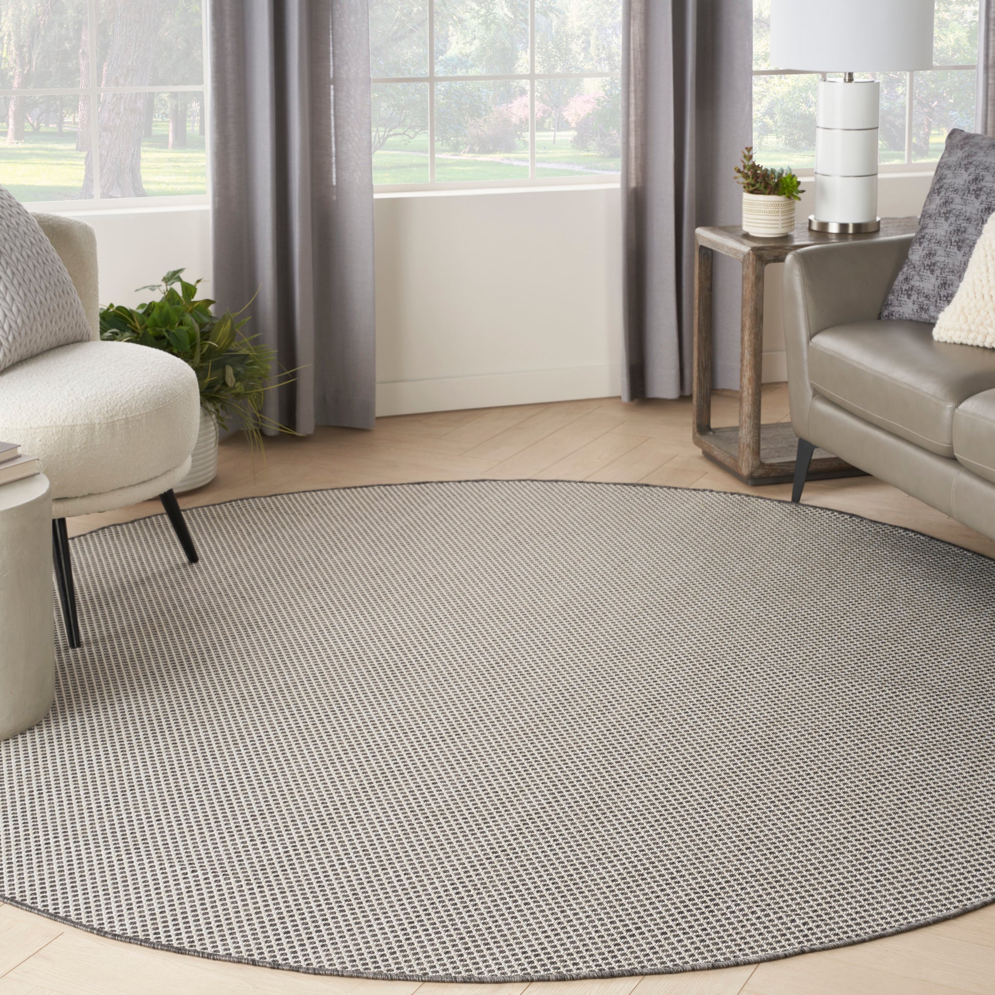 Round gray woven area rug in a modern living room with sofa, chair, and plants.