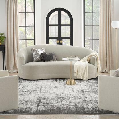 Beige curved sofa with plush cushions, cream throw, round gold side table, rug; arched black door & sheer curtains.