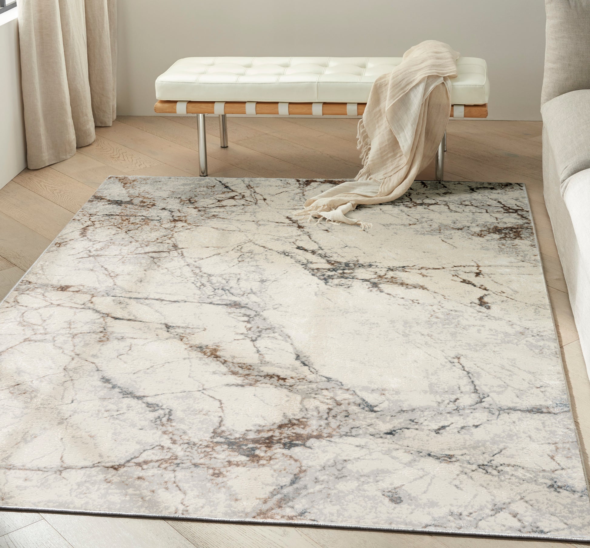 Cream area rug with gray-brown marble veining in a bright living room, white tufted bench and beige draped throw.