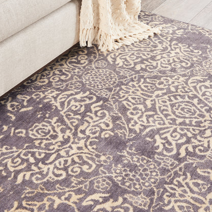 Purple and cream damask pattern rug beside a beige sofa with a cream fringed throw.