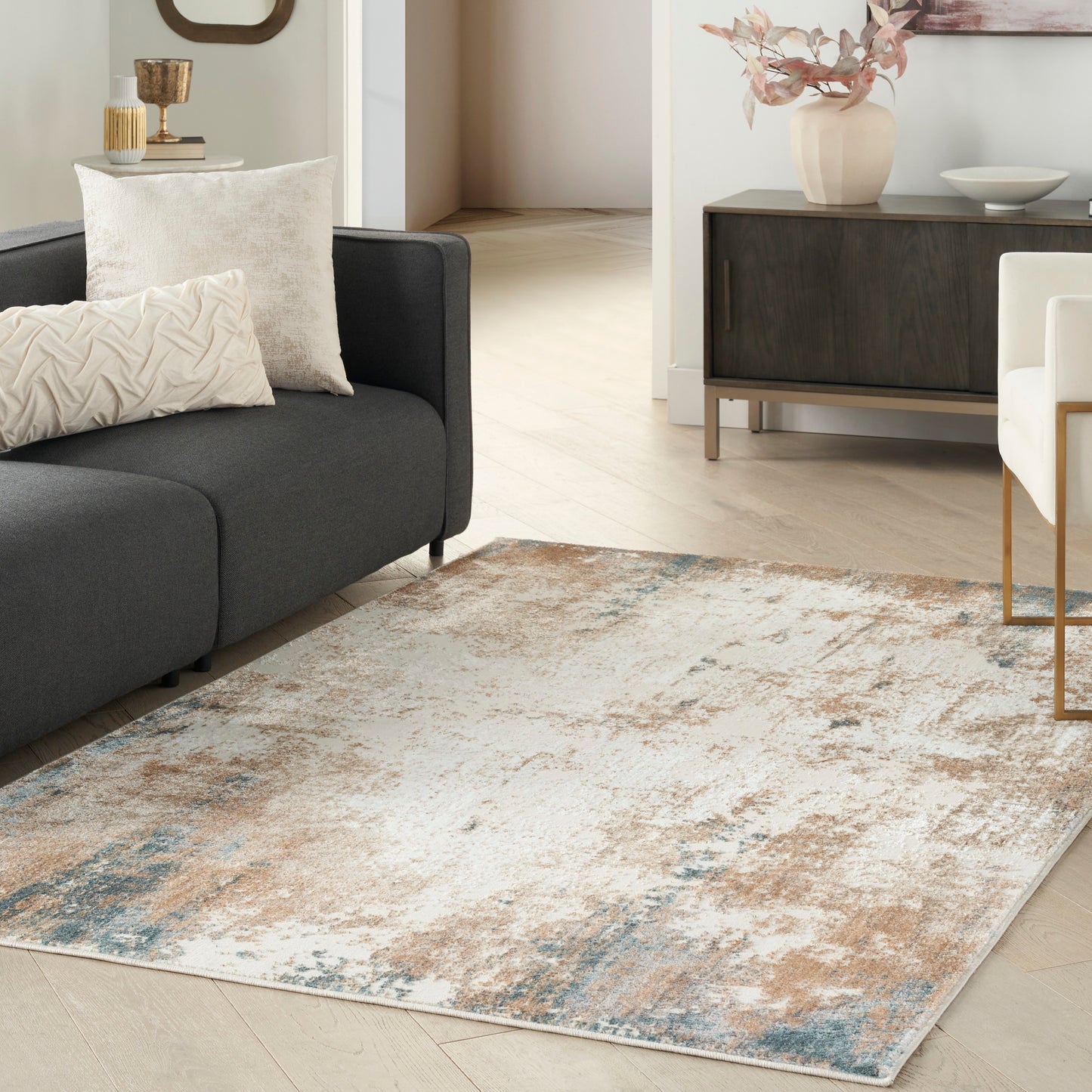 Abstract distressed area rug in beige, blue, and gray tones under a dark gray sofa in a modern living room.