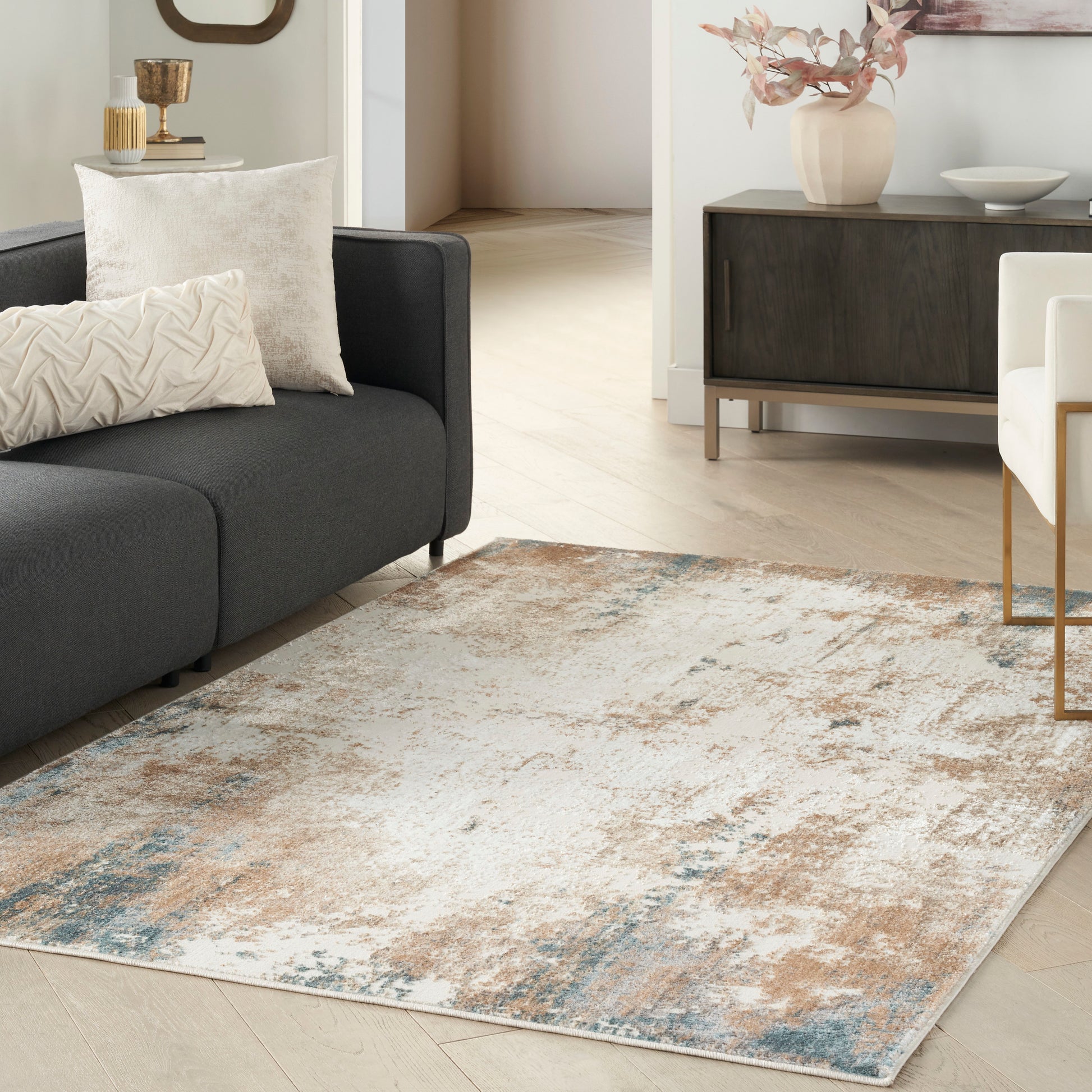 Abstract distressed area rug in beige, blue, and gray tones under a dark gray sofa in a modern living room.