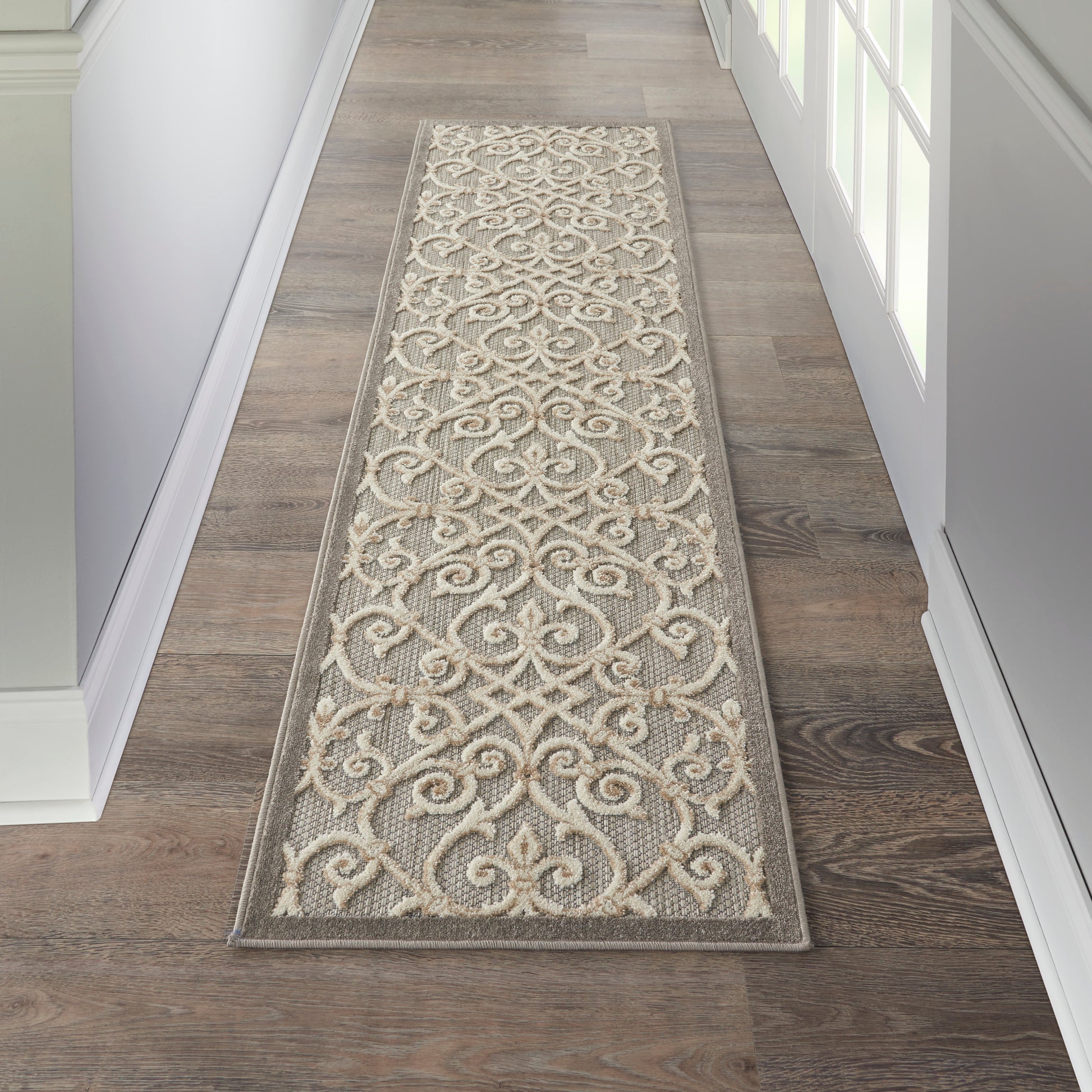 Textured beige and gray woven runner rug with ornate scrolling pattern in a narrow hallway.
