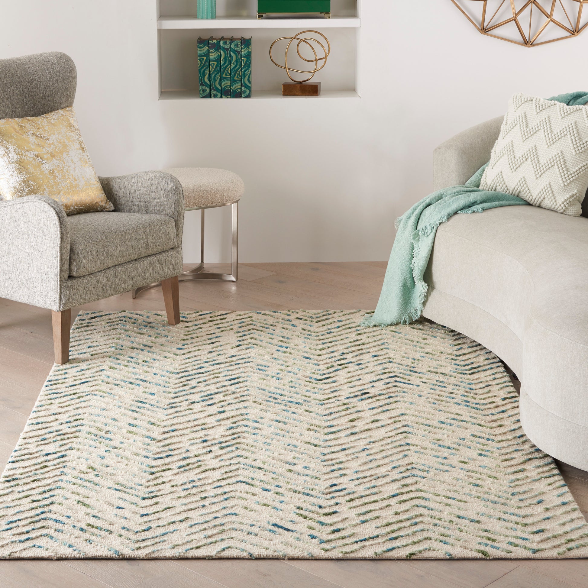 Cream rug with blue-green chevrons in a bright living room; beige sectional, gray armchair, mint throw.